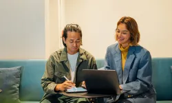 To kollegaer arbejder sammen på laptop og tablet i uformelt kontormiljø